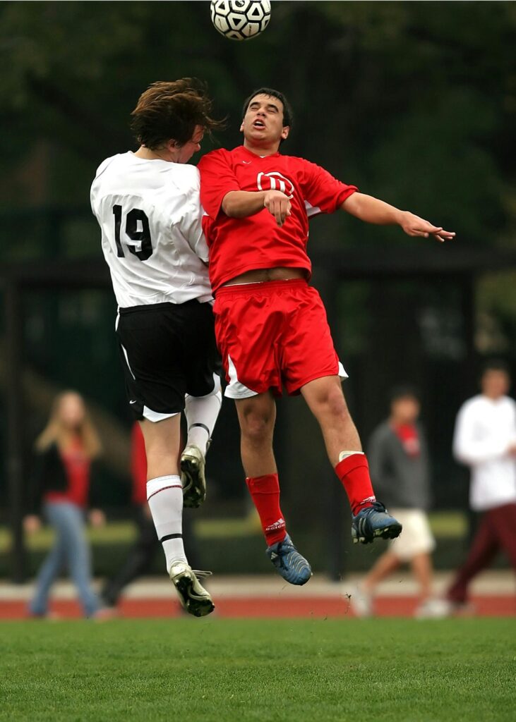 Two soccer players in mid-air challenge on a green field during a game.